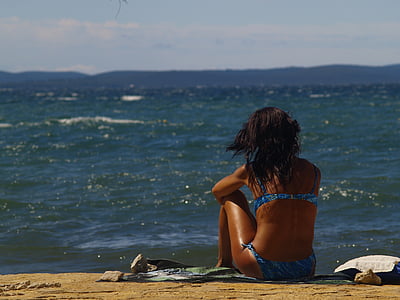 woman sitting on seashore during daytime thumbnail