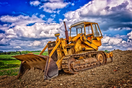 yellow payloader surrounded by plants under cloudy sky thumbnail