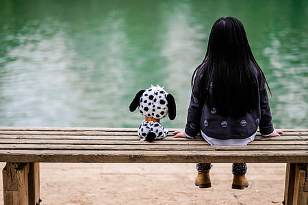 girl in black jacket and blue denim pants sitting beside dalmatian puppy plush toy during daytime thumbnail