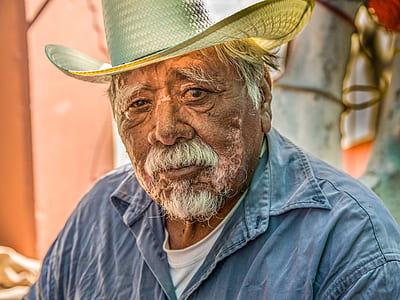 man wearing blue denim jacket and brown straw cowboy hat standing near pink painted wall closeup photography thumbnail