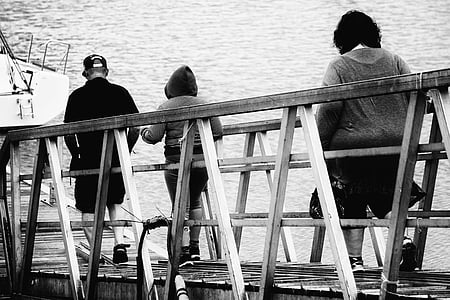 grayscale photo of man and two women crossing wooden bridge thumbnail