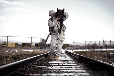 soldier walking on trail railway carrying adult solid black German shepherd thumbnail