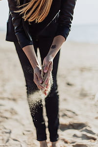 woman wearing black leather jacket and black pants holding sand on shore thumbnail