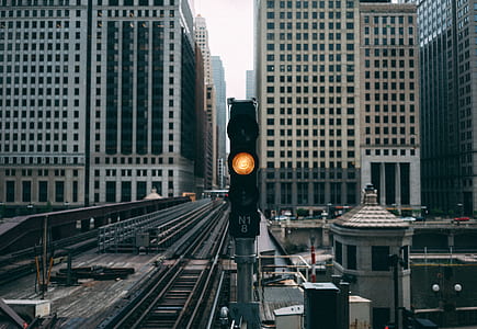 black train station stoplight displays yellow light with view of high-rise buildings during daytime photo thumbnail