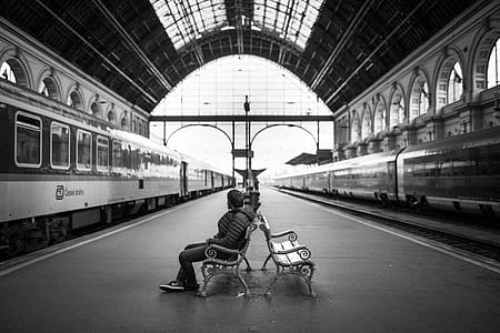 grayscale photo of man sitting on bench on train station thumbnail