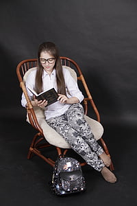 woman reading book while sitting on brown rattan chair thumbnail
