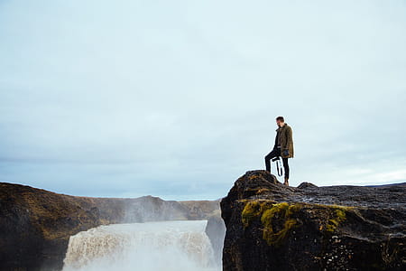 A hiker carrying a camera on a cliff by the waterfall thumbnail
