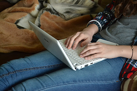 woman wearing gray long-sleeved shirt and blue jeans with white laptop on lap thumbnail