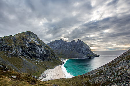 mountain coated with green grass under cloudy sky thumbnail