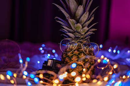 close-up photography of pineapple fruit and silver-colored sunglasses surrounded by string lights thumbnail
