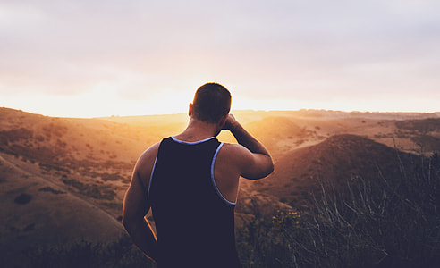 man in black tank top standing on hill during golden hour thumbnail