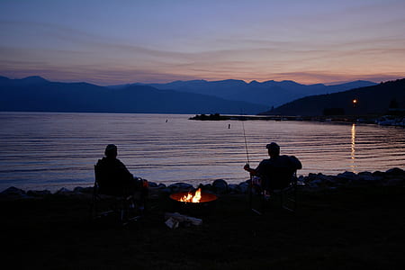 two men silhouette sitting beside body of water thumbnail