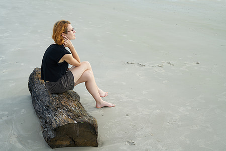 woman wearing black shorts sitting on driftwood thumbnail