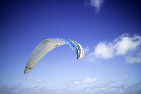 blue and white paraglider parachute under blue skies thumbnail