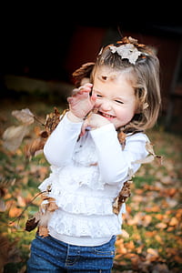 Focus Photo of Girl in White Long Sleeve Shirt With Brown Leaf on Her Head thumbnail