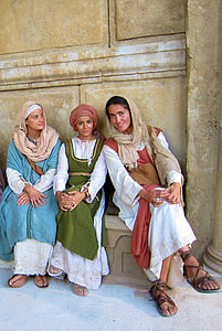 women in traditional dress sitting on brown bench next to beige painted wall during daytime thumbnail