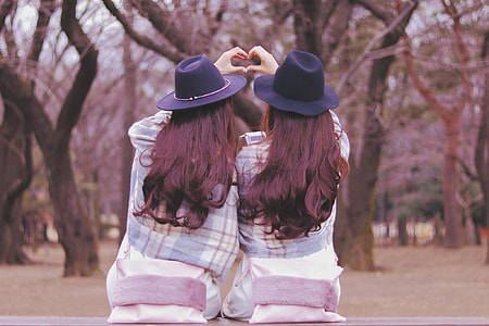 two women wearing purple hat and white and blue plaid jackets facing the trees sitting on the bench at daytime thumbnail