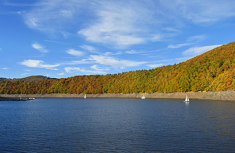 white sailboat sailing on large body of water across tree covered hill at daytime thumbnail