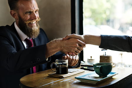 man in black suit in front of coffee on table shaking hands on person in other side thumbnail