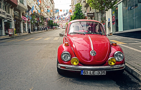 red Volkswagen Beetle car park beside concrete buildings thumbnail
