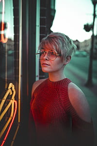 woman wearing hippie sunglasses looking on neon light signage thumbnail