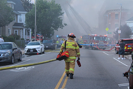 fireman carrying duffle bag walking on road surrounded by cars thumbnail
