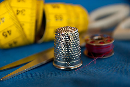 grey steel thimble near red thread spool thumbnail