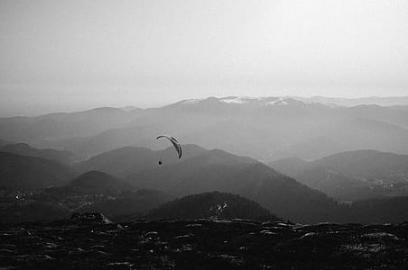 grayscale photography of person paragliding above hills thumbnail