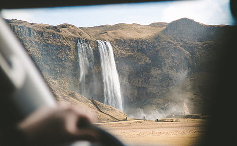 vehicle windshield overlooking waterfalls surrounded by beige cliff and hills during daytime thumbnail