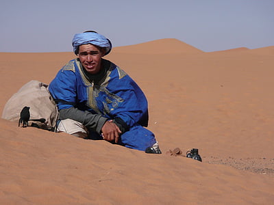 man in blue suit sitting on brown sand during daytime thumbnail