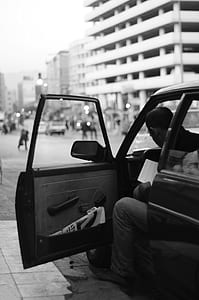 grayscale photo of man sitting in car while reading thumbnail