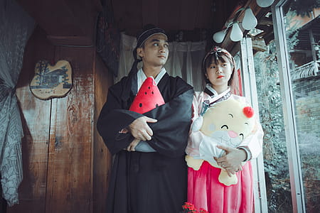 Man and Woman Holding Plush Toys Standing on Front of Brown Wall thumbnail