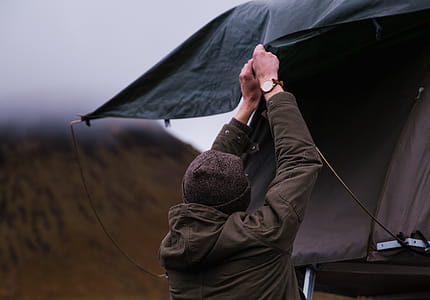 A young caucasian man wearing brown jacket setting up tent thumbnail