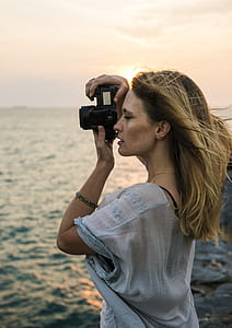woman in grey floral top holding black DSLR camera thumbnail