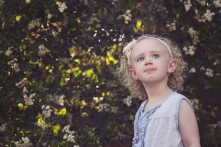 girl wearing white sleeveless dress standing in front of green leaf plant thumbnail