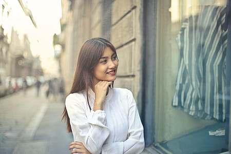 Young Asian Woman In White Shirt With Hand On Chin Doing Window Shopping On The Street thumbnail