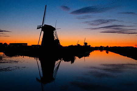 silhouette photography of windmill beside body of water thumbnail