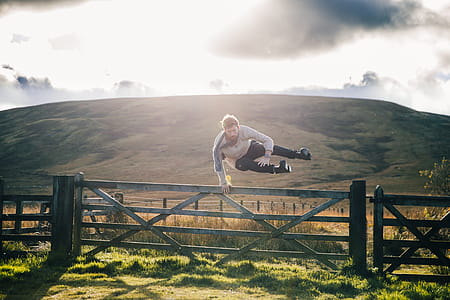 Man Jumping Fence By Field Photo thumbnail