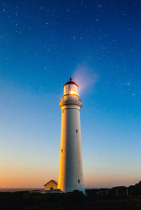 white lighthouse near trees at night time thumbnail