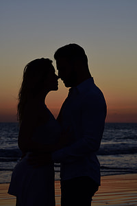 silhouette of man and woman standing side by side near beach during dusk thumbnail