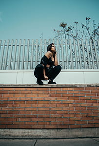 woman standing on brick fence under gray sky thumbnail