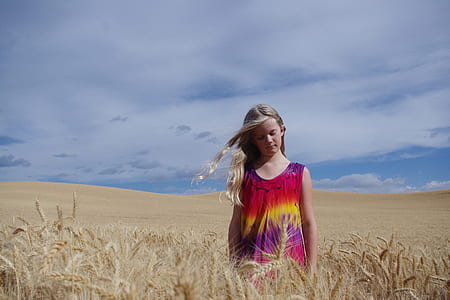 girl walking on wheat field under cloudy sky thumbnail