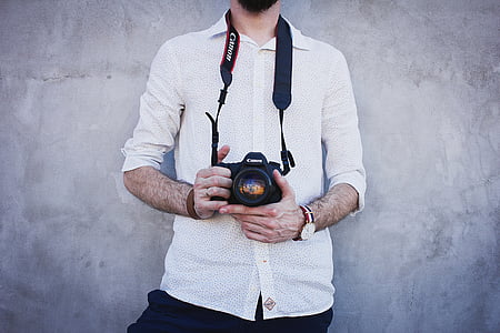 man in white dress shirt holding camera standing near wall thumbnail