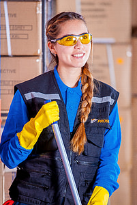 smiling woman holding gray metal rod while standing beside stacked cardboard boxes thumbnail