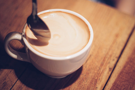 coffee in white ceramic cup and silver-colored spoon placed in brown wood surface thumbnail
