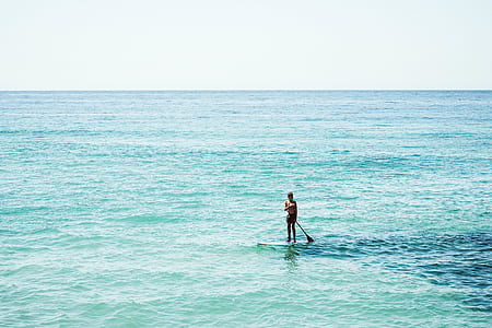 person paddling on surfboard on ocean at daytime thumbnail