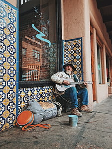 man playing guitar sitting beside wall thumbnail