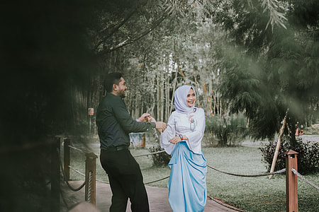 man holding hands of woman standing on wooden bridge surrounded by trees thumbnail