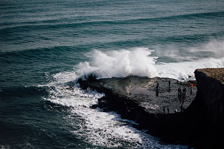 group of people standing on rock near sea water waves during daytime thumbnail