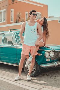 woman sitting on green vehicle's hood while man standing in front of her and they are both smiling at daytime thumbnail
